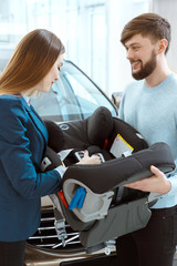 Beautiful loving couple buying car seat for children at the car dealership center