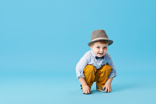 Portrait of happy joyful  little boy isolated on blue background. Toddler child in hat and fashionable suit smiling and have a fun. Copy space for text left side