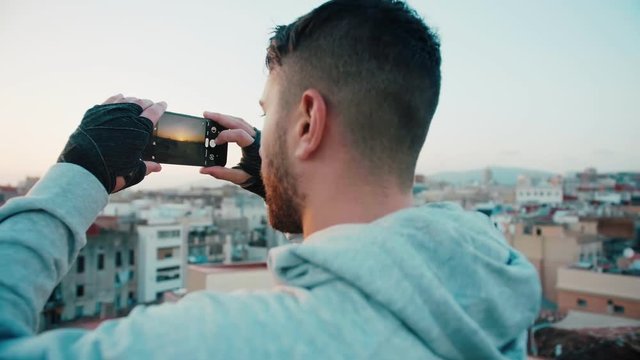 Sport attractive man in good shape taking a smartphone or mobile phone photo or picture of sunset or sunrise on a city rooftop after or before training To capture the moment and apply filter and share
