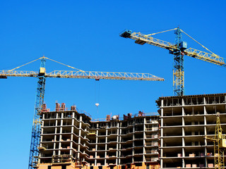 Two building cranes and building under construction. Construction Background. Construction site with cranes on sky background.