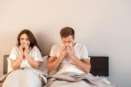 Young couple in the bed. Sick man and woman are blowing noses and suffering from ill in the bedroom