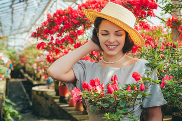 Beautiful adult girl in an azalea greenhouse reading a book and dreaming in a   beautiful retro dress