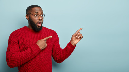 Surprised excited black man points aside with fore fingers on blank space, tells emotionally what...