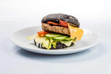 cheeseburger with black bread, beef cutlet, bacon, tomatoes and cheese slices, seasoned with sauce and green salad for a restaurant menu on a white isolated background