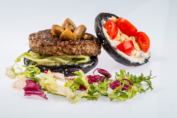 cheeseburger with black bread, beef cutlet, bacon, tomatoes and cheese slices, seasoned with sauce and green salad for a restaurant menu on a white isolated background