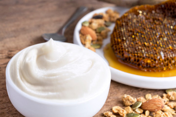 Healthy flavored yogurt in ceramic bowl with granola and honey comb on the wood background.