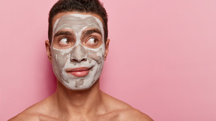 European man with thoughtful expression, has facial treatments, thinks about buying new cosmetics,...