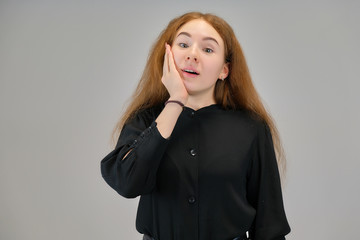 Concept portrait of a cute pretty teenager girl with red hair on a gray background smiling and talking.