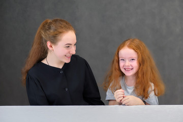 Fototapeta na wymiar Concept portrait of two cute pretty girls sisters with red hair on a gray background smiling and talking.