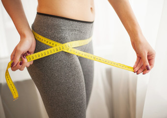Slim young woman measuring her thin waist with a tape measure