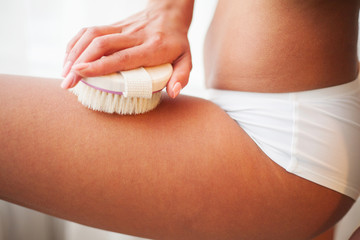 Woman's arm holding dry brush to top of her leg. Cellulite treatment, dry brushing