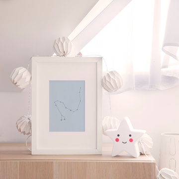 Stylish and cute nursery interior with mock up photo frame , star and cotton lapms on the wooden shelf. Bright and sunny room with white background wall. 