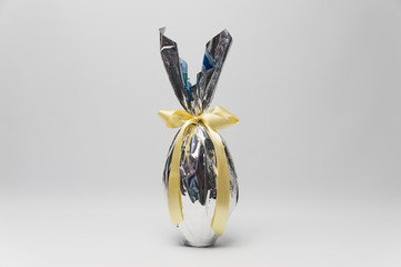 Homemade Easter egg in beautiful silver packaging with yellow ribbon. Isolated on white background. Horizontal image with space for text.