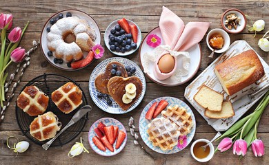 Easter festive dessert table with hot cross buns, cakes, waffles and pancakes. Overhead view