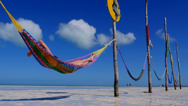 Happy young woman on vacation laying and resting in hammock at sunset in hot summer on Mexico beach