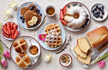 Easter festive dessert table with hot cross buns, cakes, waffles and pancakes. Overhead view