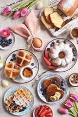 Easter festive dessert table with hot cross buns, cakes, waffles and pancakes. Overhead view