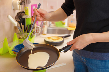 Obraz na płótnie Canvas A woman prepares pancakes, pours the dough on a hot frying pan. Holiday Maslenitsa.