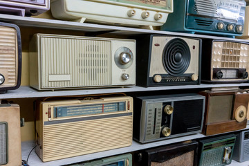 Retro broadcast radio receivers on wooden shelf against yellow background.