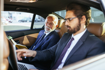 Senior businessman and his assistant sitting in limousine and working together.