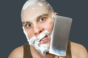 A guy with a beard and a axe in his hand, with foam and gel on his face shaves in the morning at...