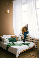 Young woman sitting on sill near big window in bedroom