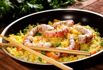 Cooked rice with shrimps, curry and vegetables in a pan with chopsticks on the wood brown bamboo background.