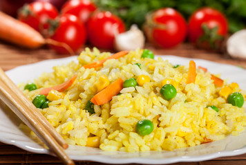 Cooked rice with curry and vegetables in a plate with chopsticks on the wood brown bamboo background.
