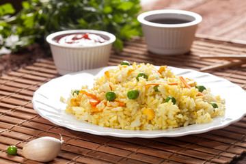 Cooked rice with curry and vegetables in a plate with sauces and chopsticks on the wood brown bamboo background.