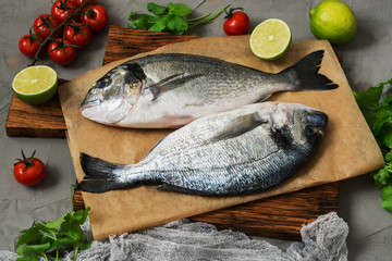Fresh dorado fish on a cutting board with lime, tomatoes and greens.
