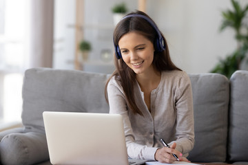 Smiling woman in headphones using laptop, writing notes