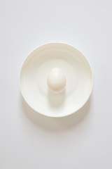 one fresh white egg lies on a white plate on a light background. Copy space for lettering and design
