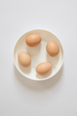 four fresh brown eggs lie on a white plate on a light background. Space to copy the inscriptions and design