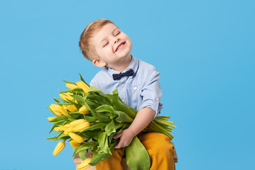 Adorable smiling child with spring flower bouquet looking at camera isolated on blue. Little...