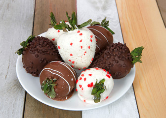 Variety of Chocolate covered strawberries on a plate. Dark, white and milk chocolate on a wood table multiple colored slats. side view