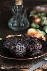 cut fried black pudding, oil and vegetables in porcelain dish on wood
