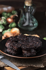 cut fried black pudding, oil and vegetables in porcelain dish on wood