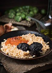 Homemade rice stew with black pudding and tomato in porcelain dish on wood