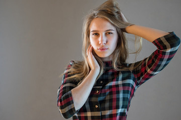 Fototapeta premium young blonde girl in plaid dress touches her hair. woman poses for camera demonstrating natural beauty without cosmetic and makeup. Tender emotions and coquetry