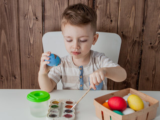 Little boy painting colorful eggs for easter on wooden background