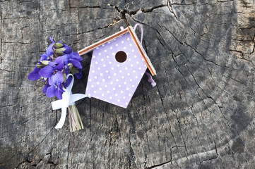 Bouquet of violet flowers and decorative birdhouse on wooden background. Spring postcard. March 8.