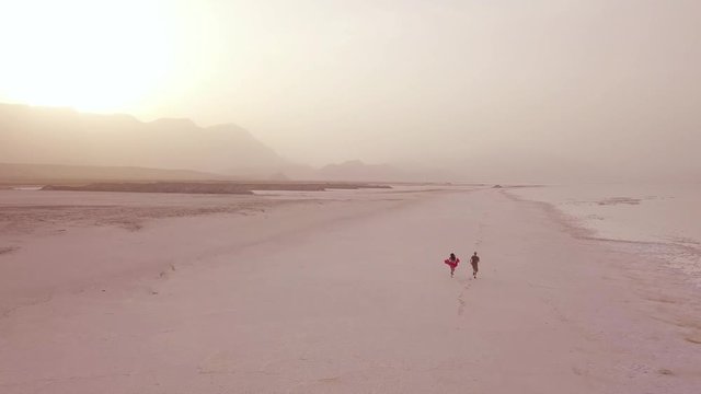 Aerial over a model released couple running and having fun on a wide sandy beach on the coast of Djibouti.