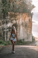Fototapeta na wymiar beautiful woman with long blonde hair in blue glasses, white shirt and denim shorts posing on backgraund of rocks in Bali