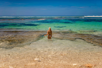 beautiful woman with long blonde hair in dark swimwear posing on the sunny tropic beach in Bali