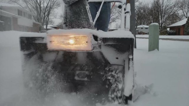 Close up of electric corded snowblower with light being push through thick layer of snow being cleared from sidewalk or path.