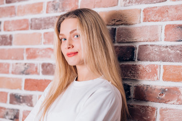 Happy cheerful young lovely blonde woman smiling and looking at the camera near brick wall