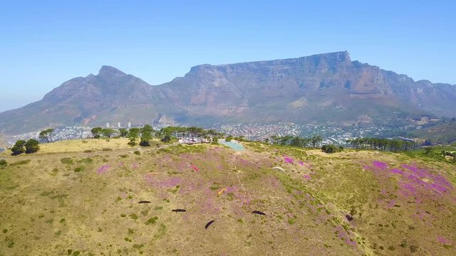 Drone aerial over paragliding and paragliders with Table Mountain Cape Town, South Africa, in background.