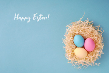 Happy Easter greeting card; Colored eggs in a hen nest. - obrazy, fototapety, plakaty