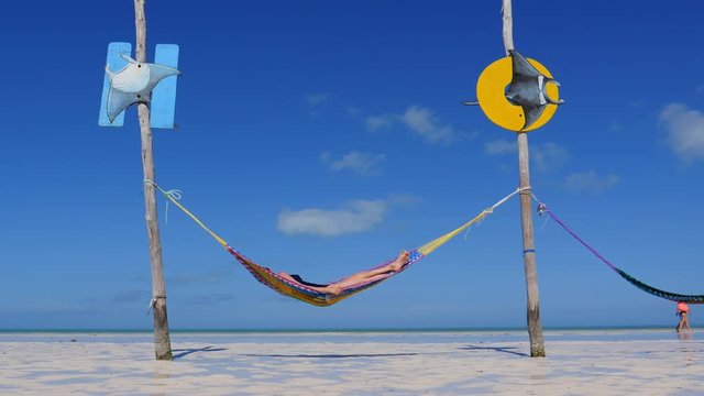 Happy young woman on vacation laying and resting in hammock at sunset in hot summer on Mexico beach