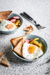Breakfast with French fries, fried egg, sausage and toast on the table
